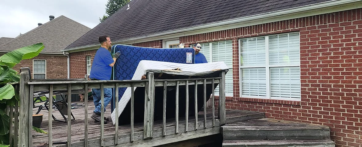 Men carrying mattress off back deck