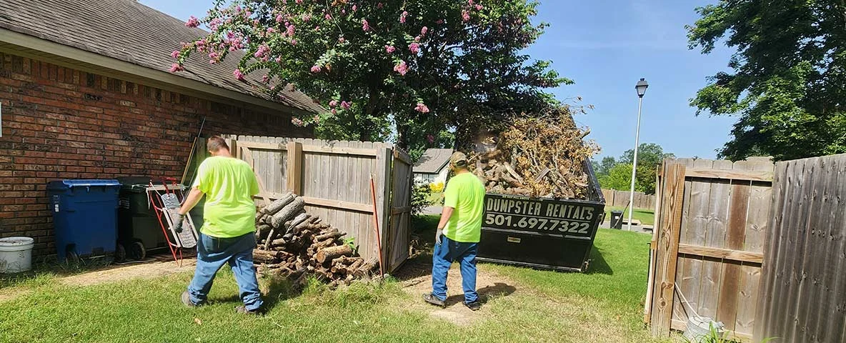 Workers loading wood and limbs into a dumpster